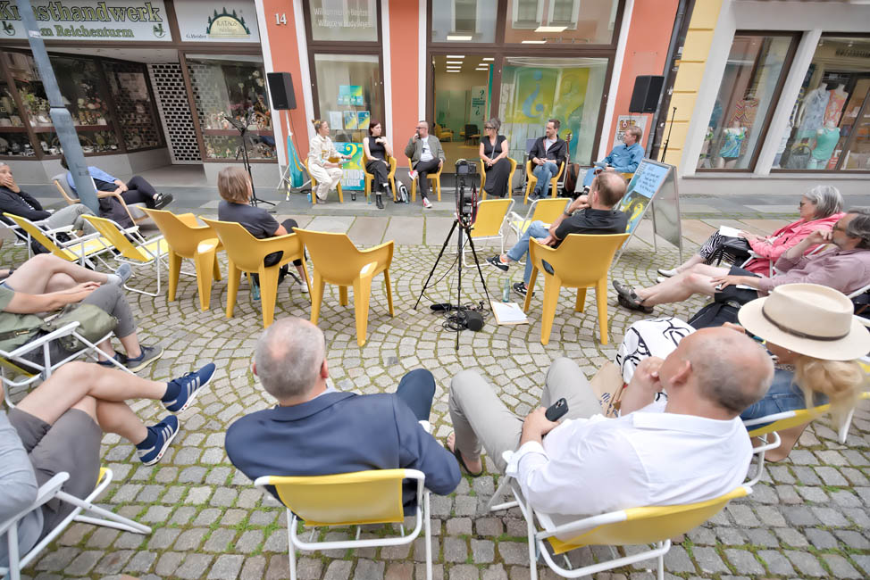 Personen auf Stühlen hören einer Gruppe von Personen zu