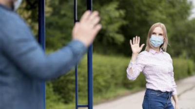 Zwei Menschen mit Maske winken sich zu